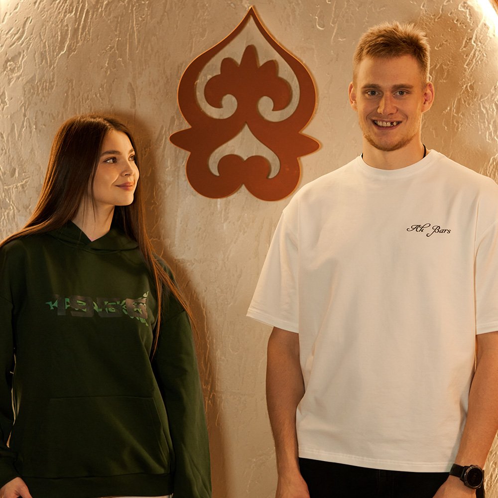 Ak Bars drop 2 — a couple against an ornament wall in white and green club garments