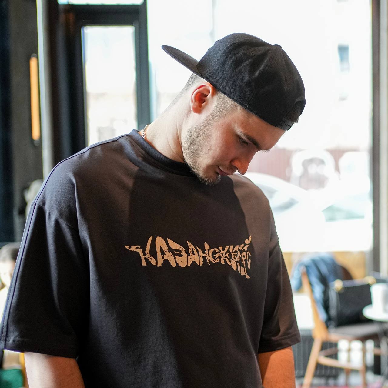 Ak Bars drop 1 — model leaning on a rail in a cream tee