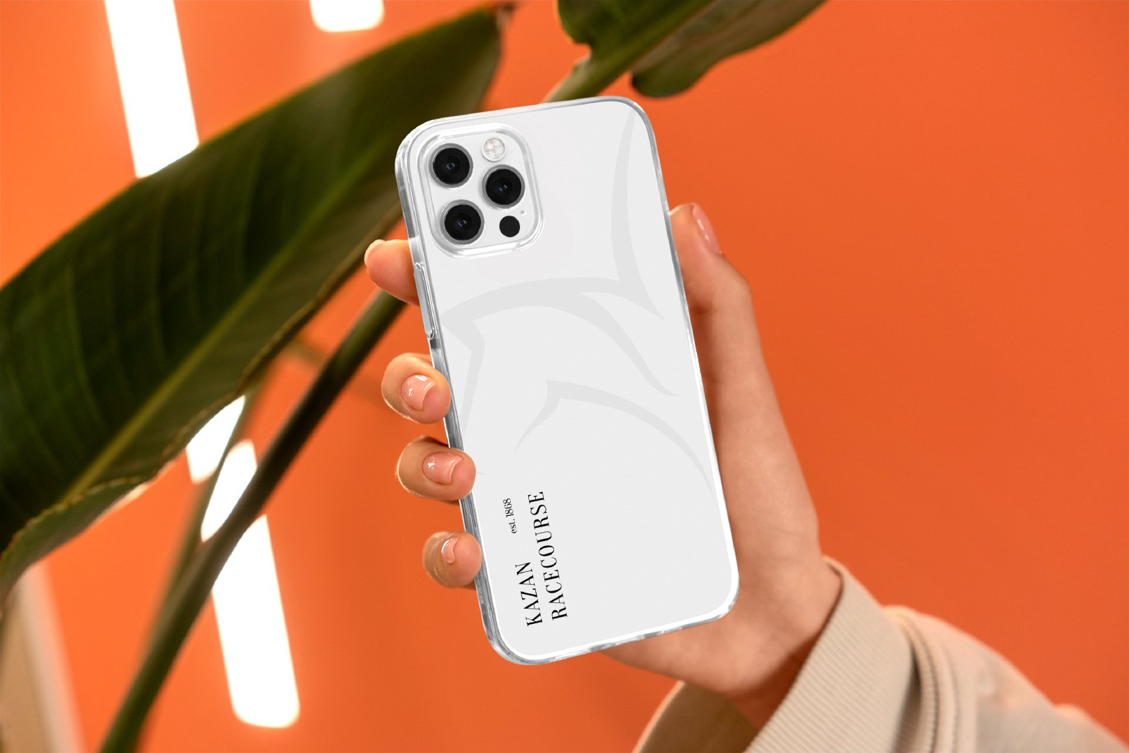 Hand holding a white branded phone case with the vertical Kazan Racecourse wordmark, against an orange backdrop