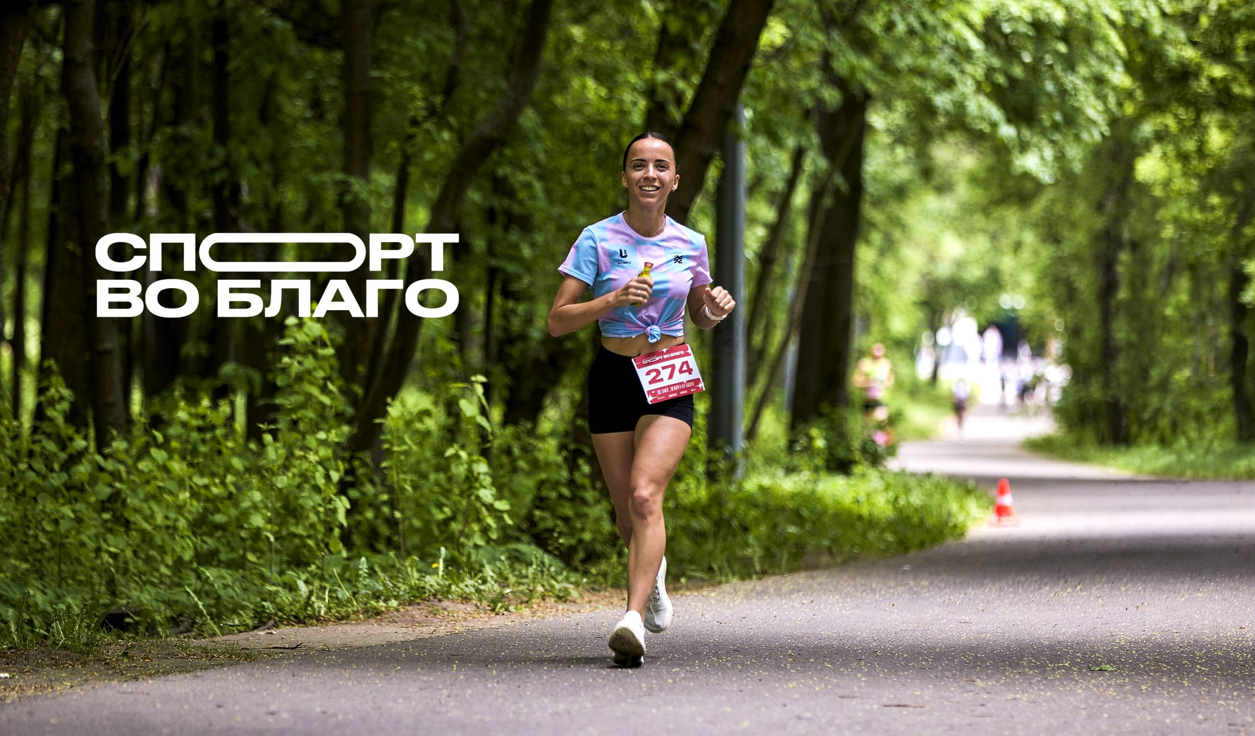 A runner on a tree-lined park path at a Sport for Good charity race, the event logotype overlaid